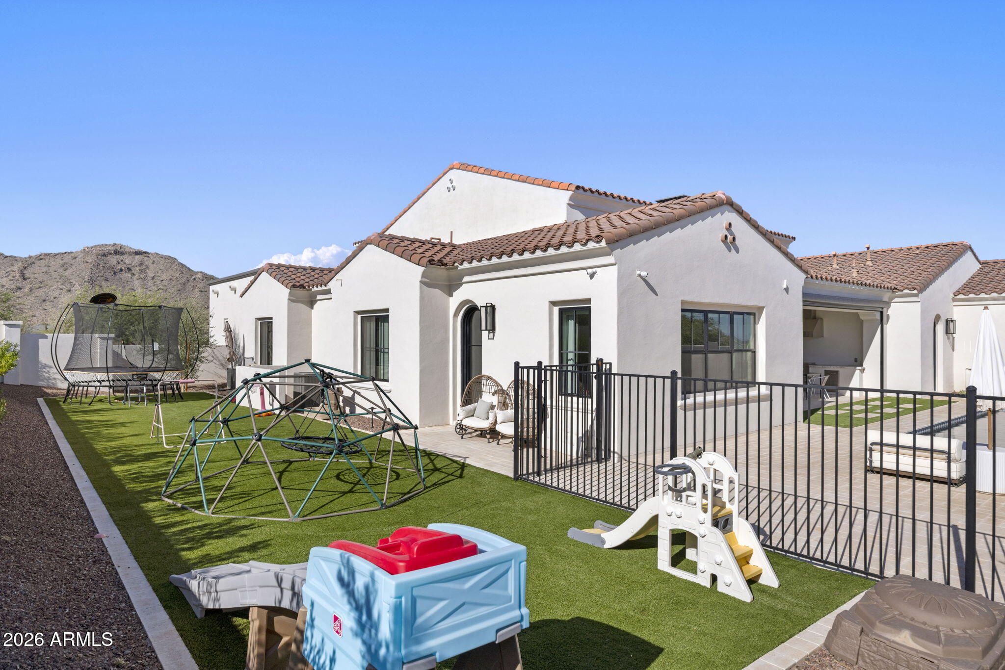Rear exterior of stucco home with tiled roof, fenced patio, and children's play equipment.