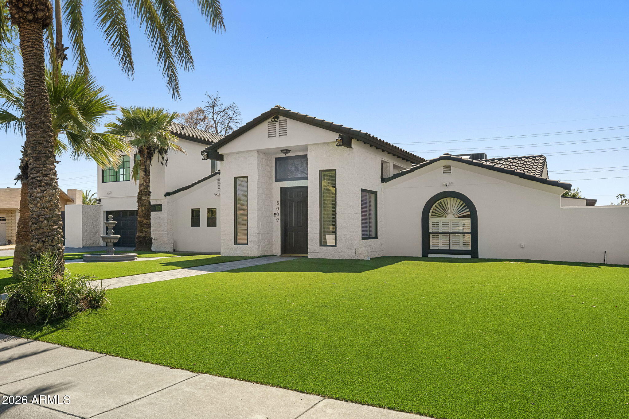 White stucco home with dark tile roofs, palm trees, and a broad manicured lawn.