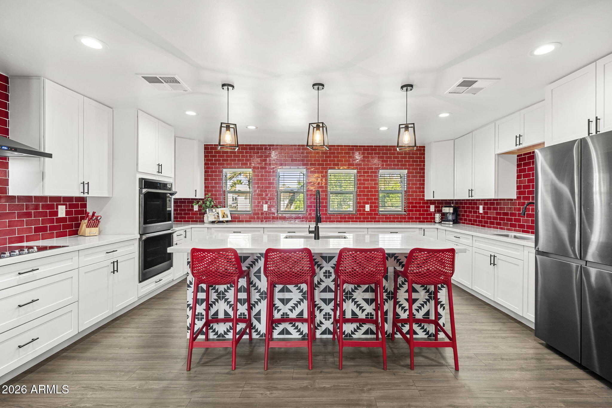 Modern kitchen with red tile walls, white cabinetry, and a patterned island lined with red stools.
