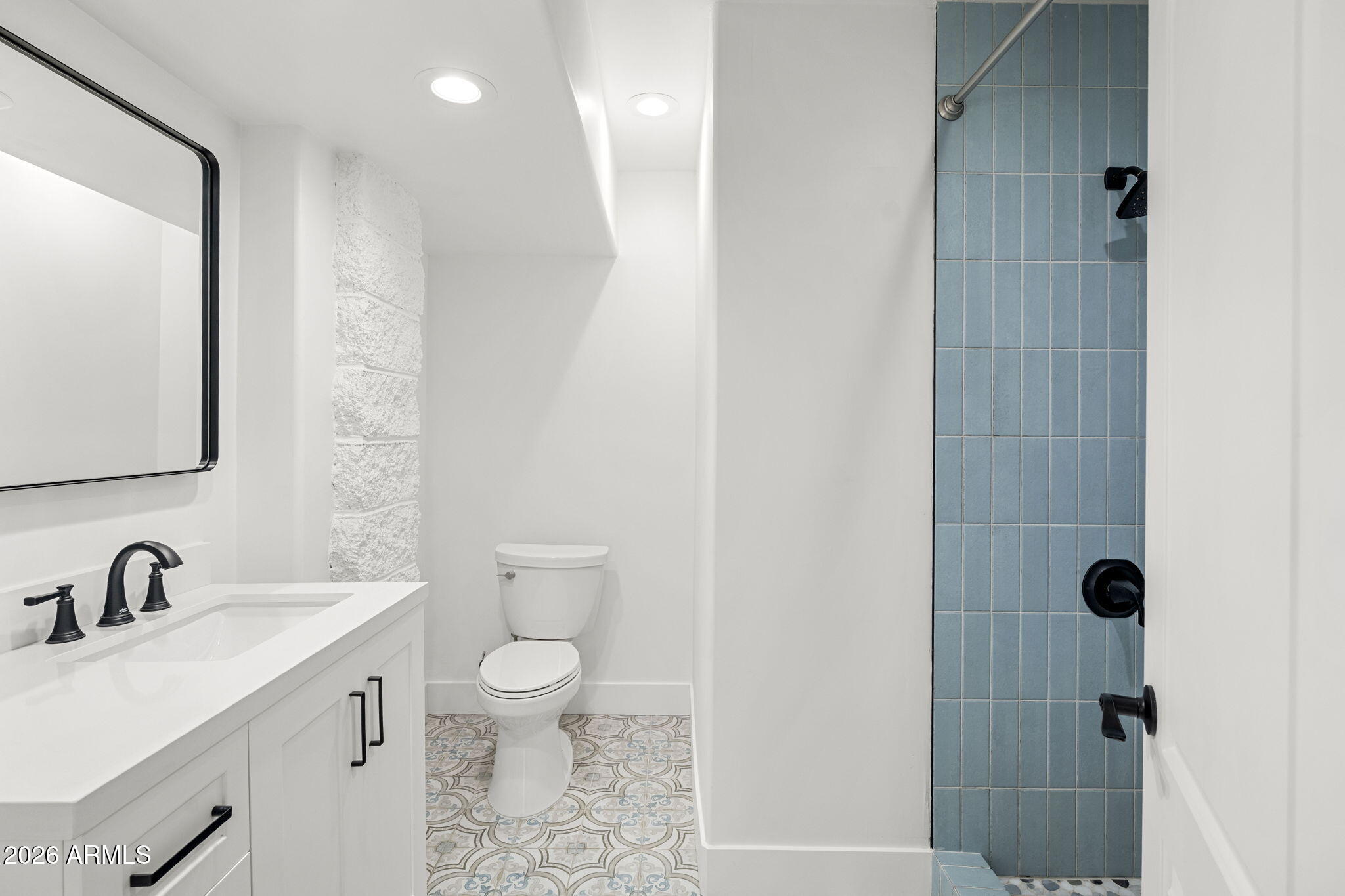 Bathroom with a blue-tiled shower, patterned floor, and white vanity with black fixtures.