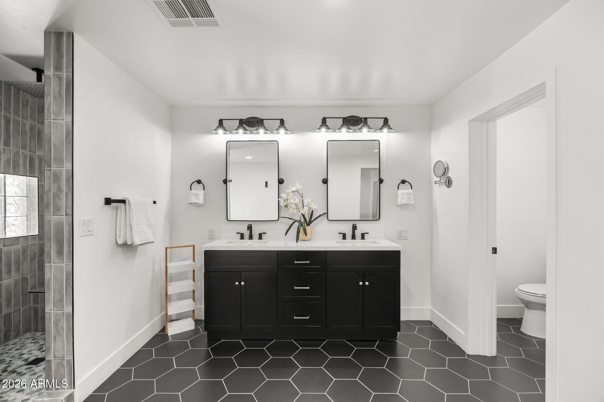 Bathroom with a black double vanity, two mirrors, hexagonal floor tiles, and a gray tiled shower.
