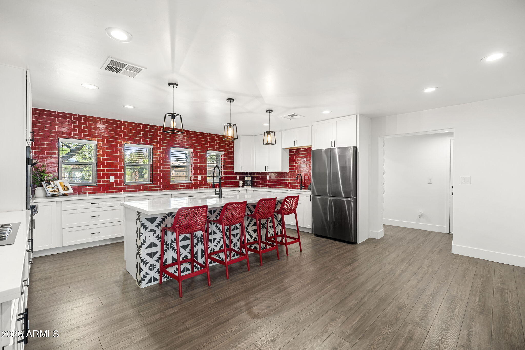 Kitchen with a red tile backsplash and a patterned island lined with red bar stools.