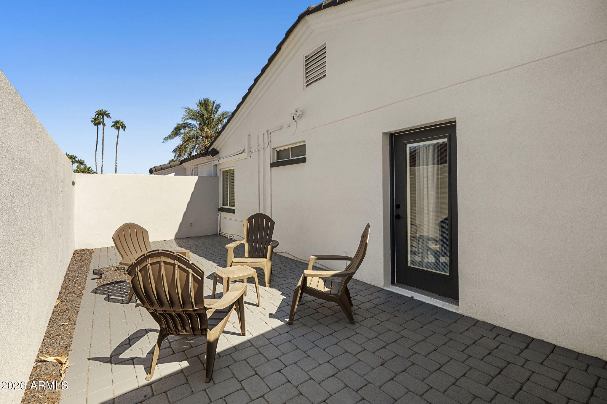Furnished paver patio with brown chairs and a table beside a stucco house.