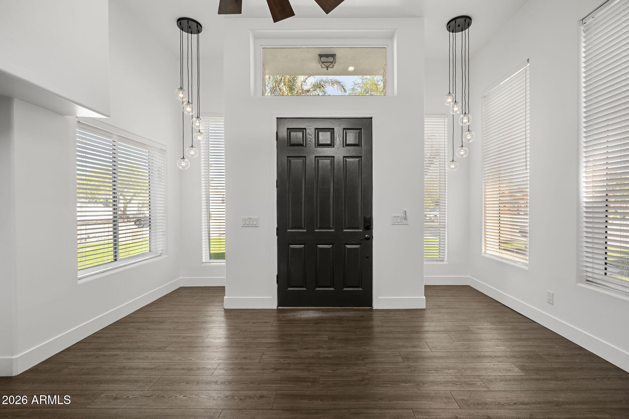 Empty entry foyer with a black paneled door, tall windows, globe pendants, and dark wood-look flooring.