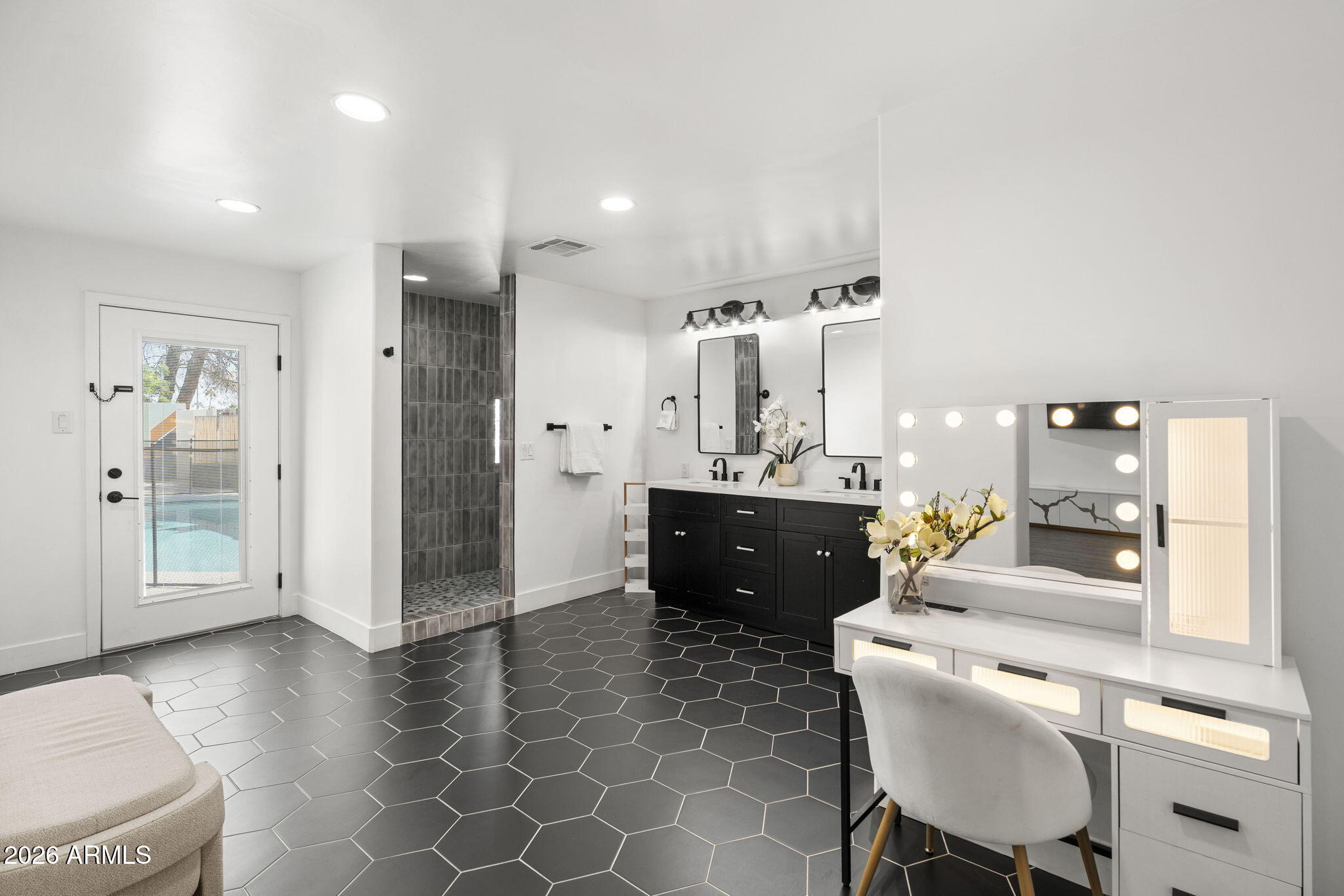 Bathroom with a black double vanity, dark hexagonal tile, walk-in shower, and illuminated makeup vanity.