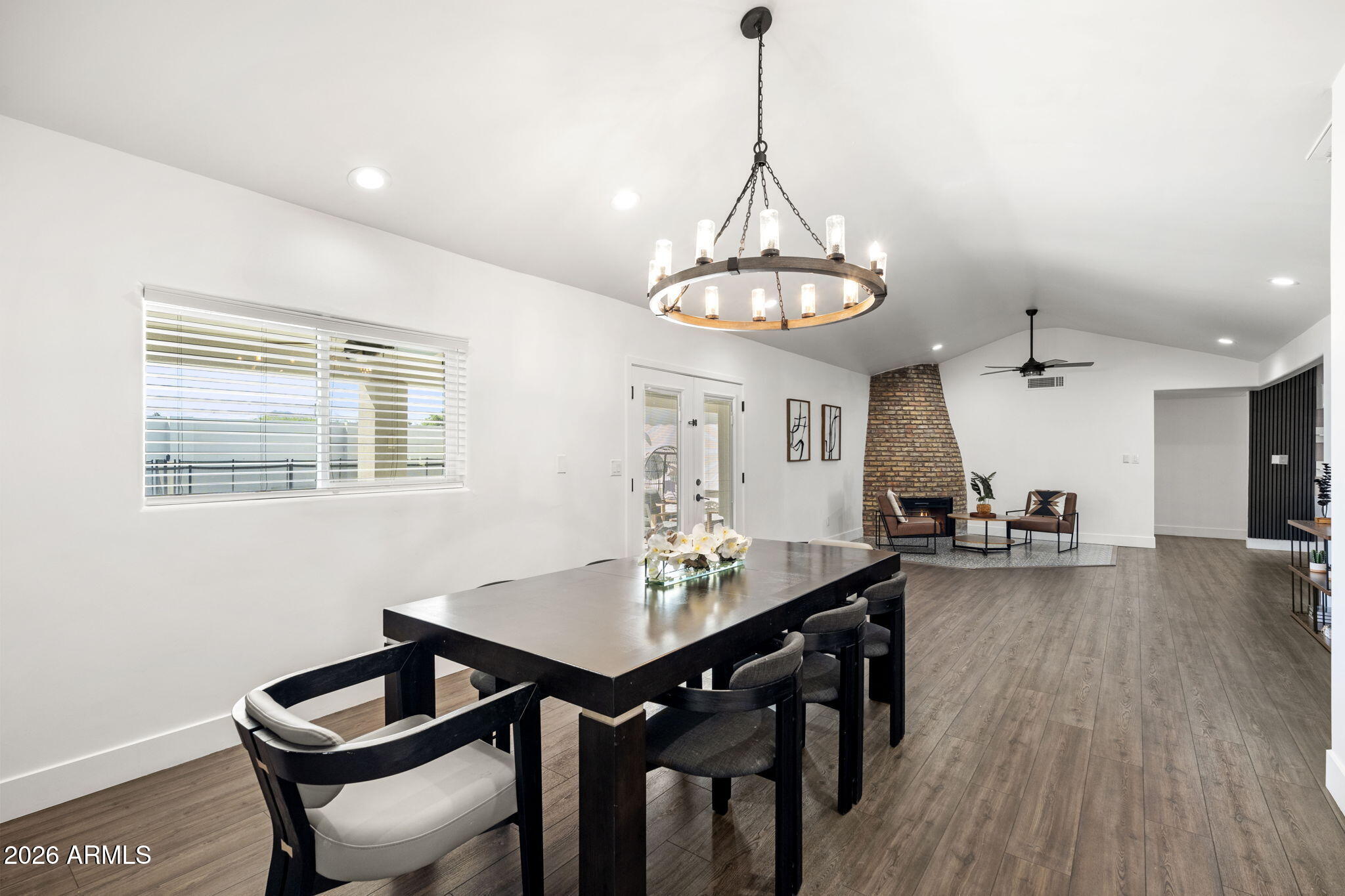 Open dining and living area with a circular chandelier, dark dining table, and brick fireplace.