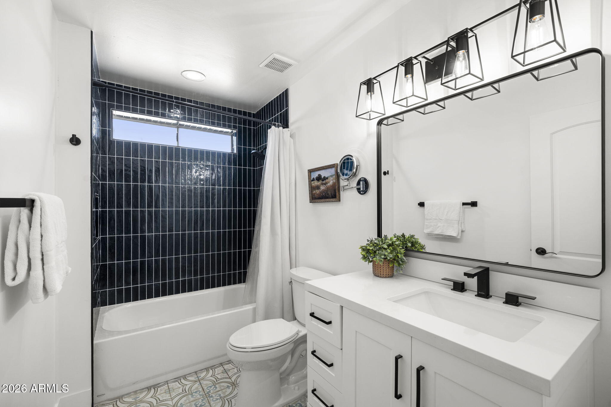Bathroom with dark tiled tub-shower, white vanity, black fixtures, and patterned floor tile.