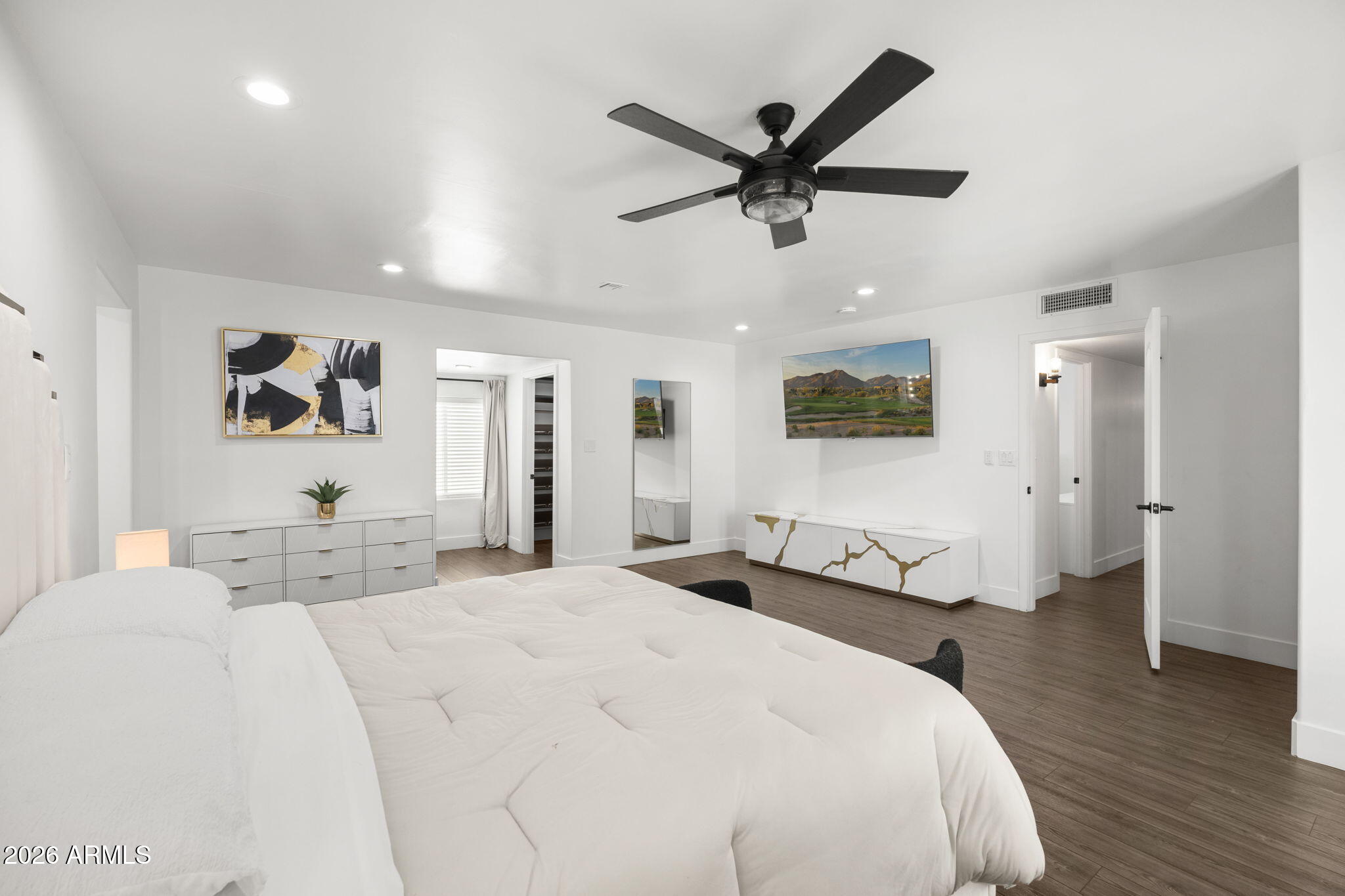 Furnished bedroom with a large white bed, black ceiling fan, and modern white dressers.