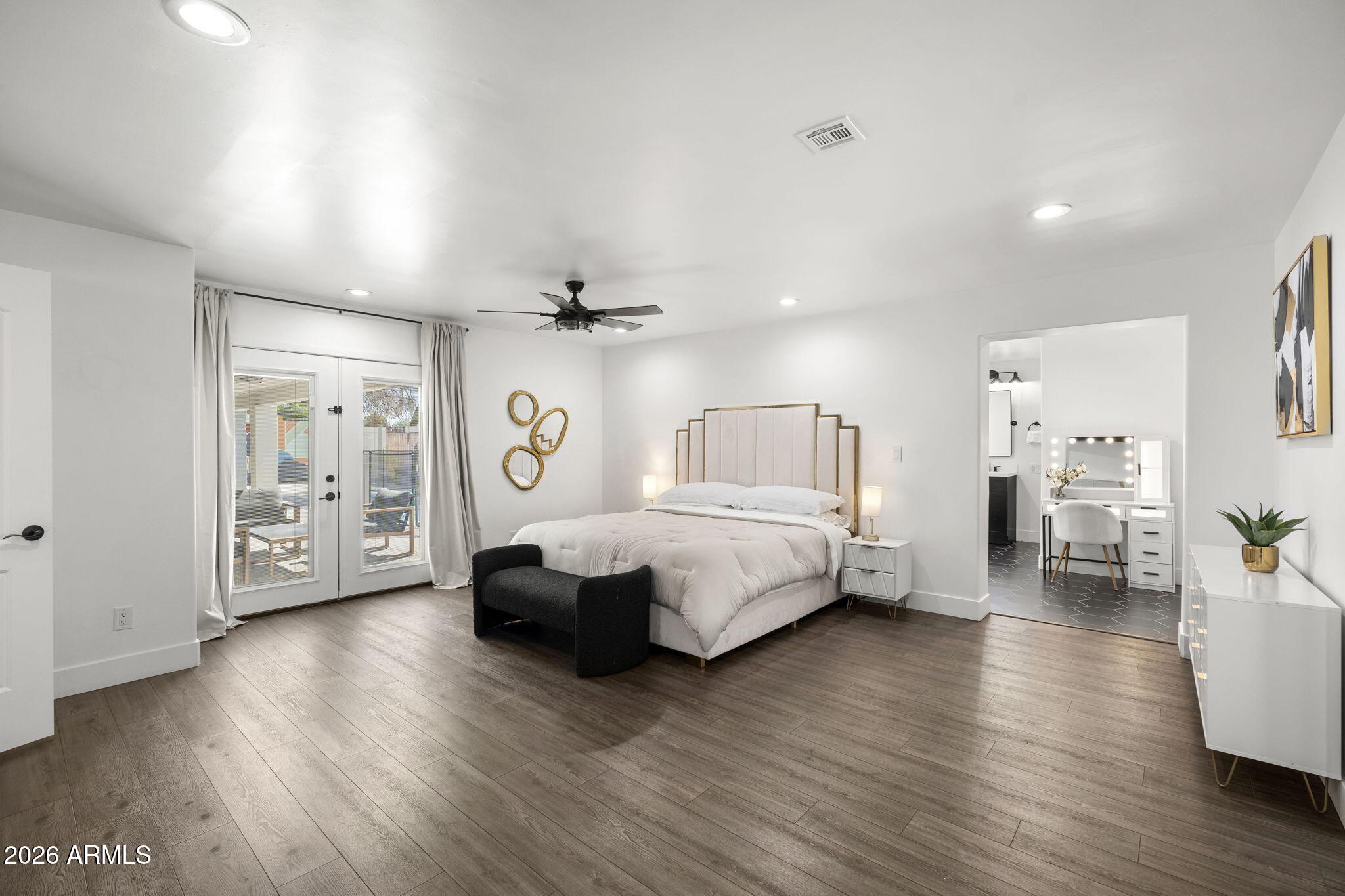 Staged bedroom with a large bed, black bench, patio doors, and an adjoining bathroom vanity.