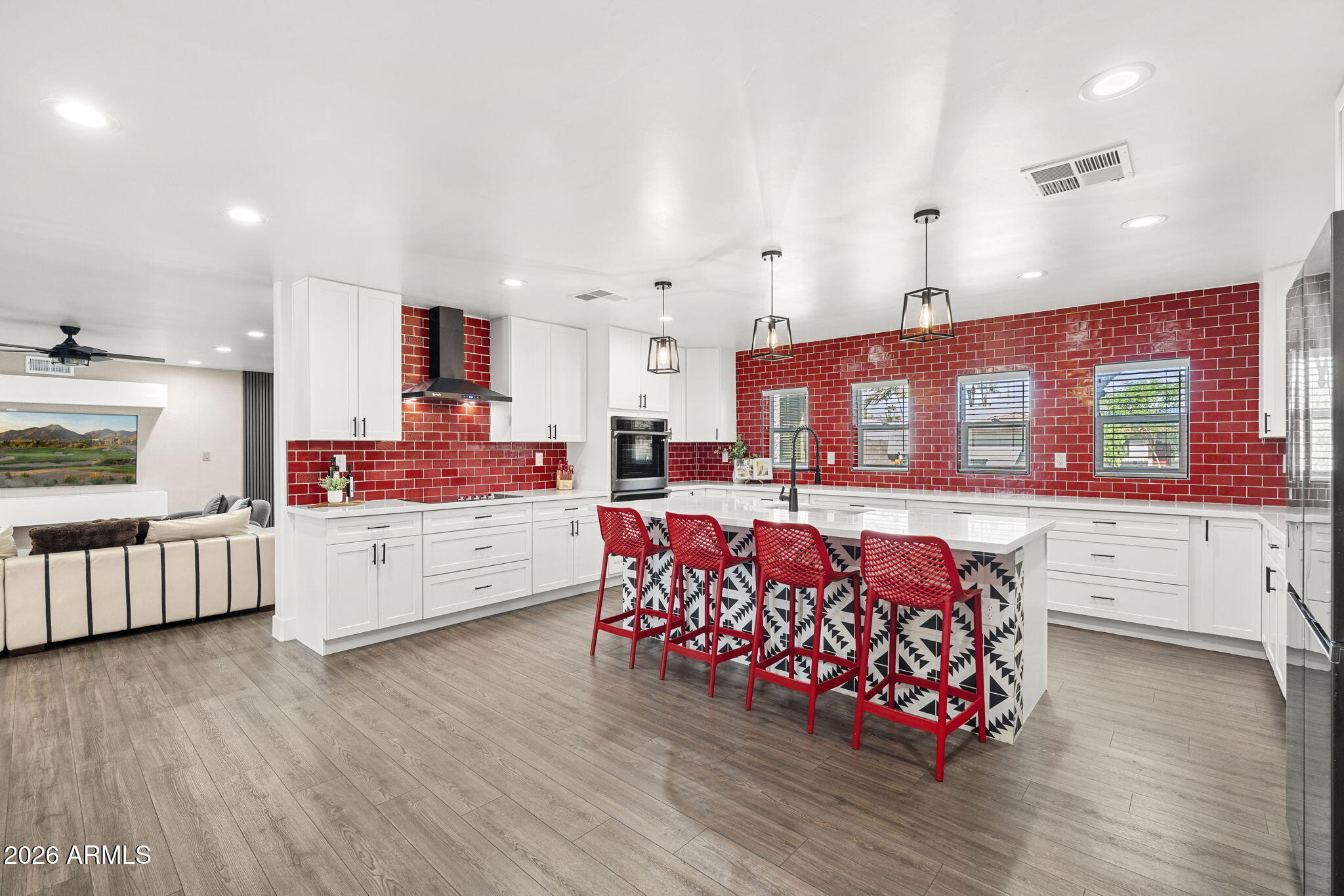 Kitchen with red tile backsplash, patterned island, and red bar stools opening onto a living area.