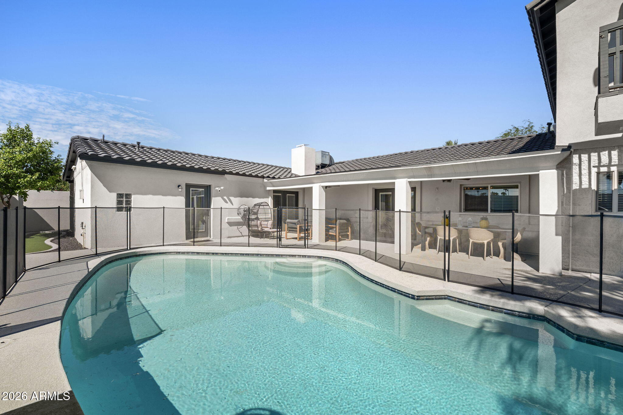 Backyard swimming pool with a black safety fence and covered patio with outdoor seating.