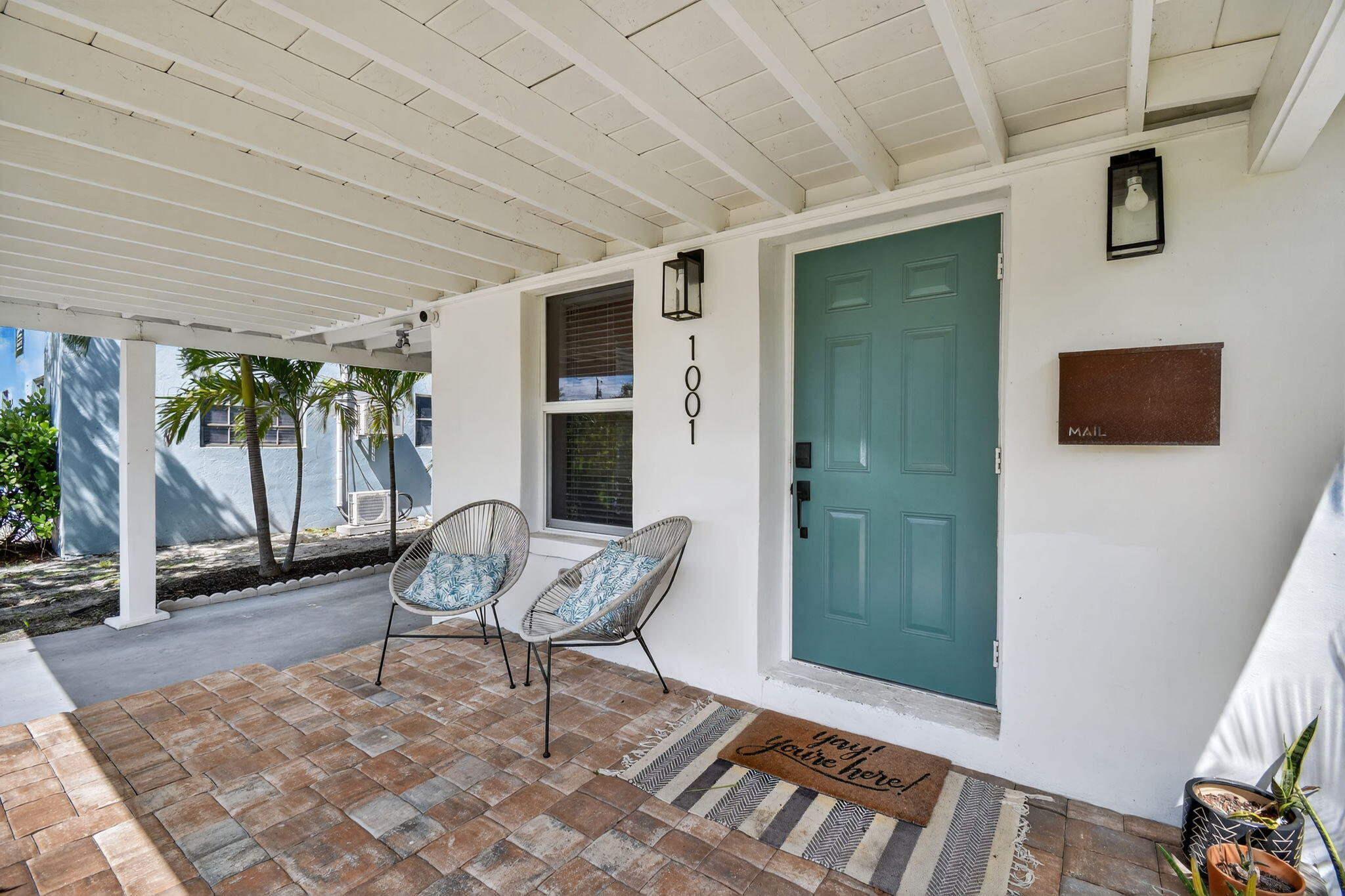 Covered front porch with a teal door, brick pavers, and two cushioned chairs.