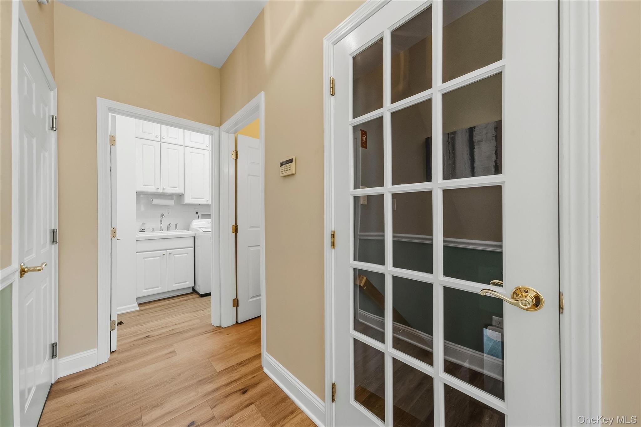Hallway with glass-paneled door and view into a white laundry room.