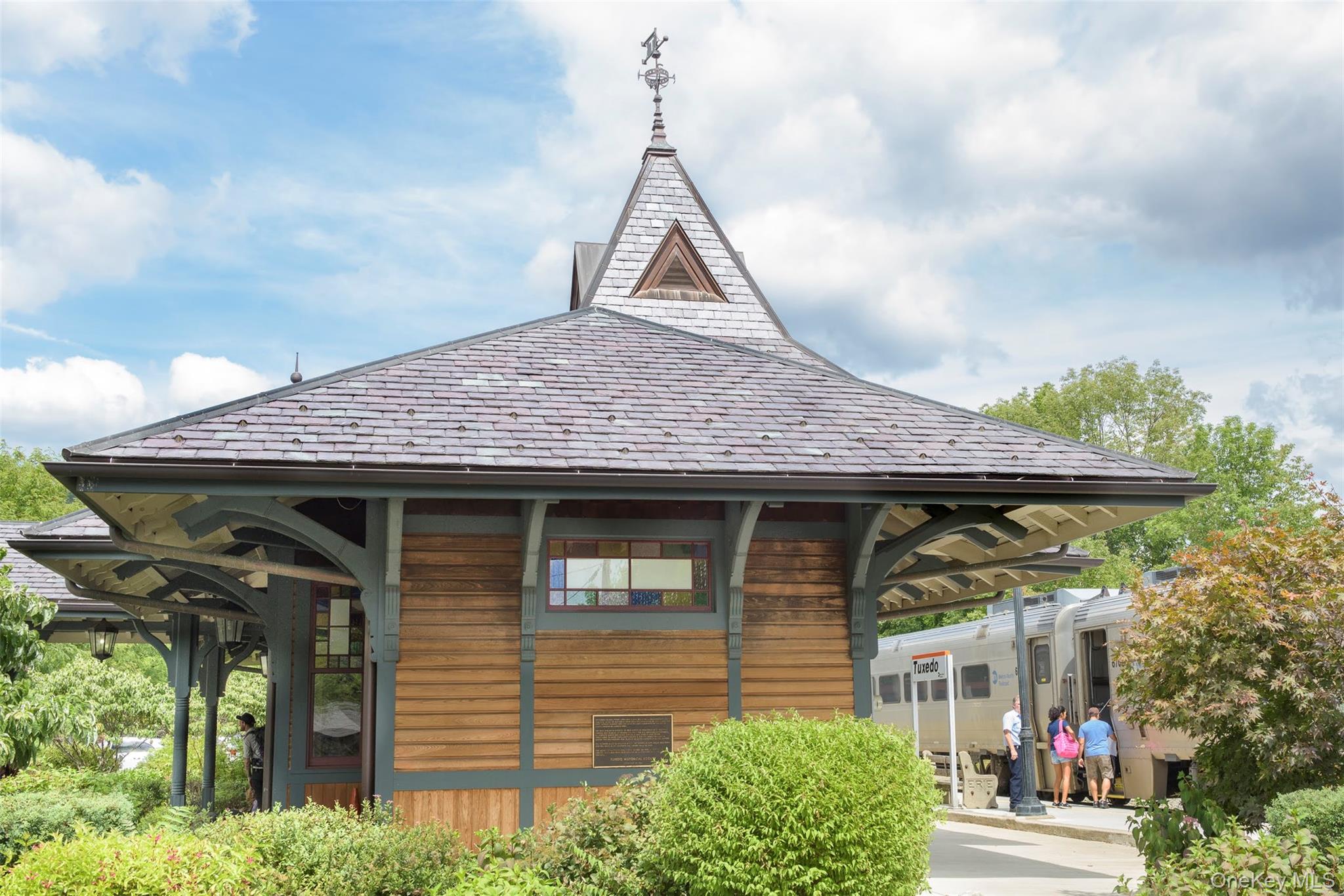 Historic Tuxedo train station beside a passenger train, with travelers boarding.