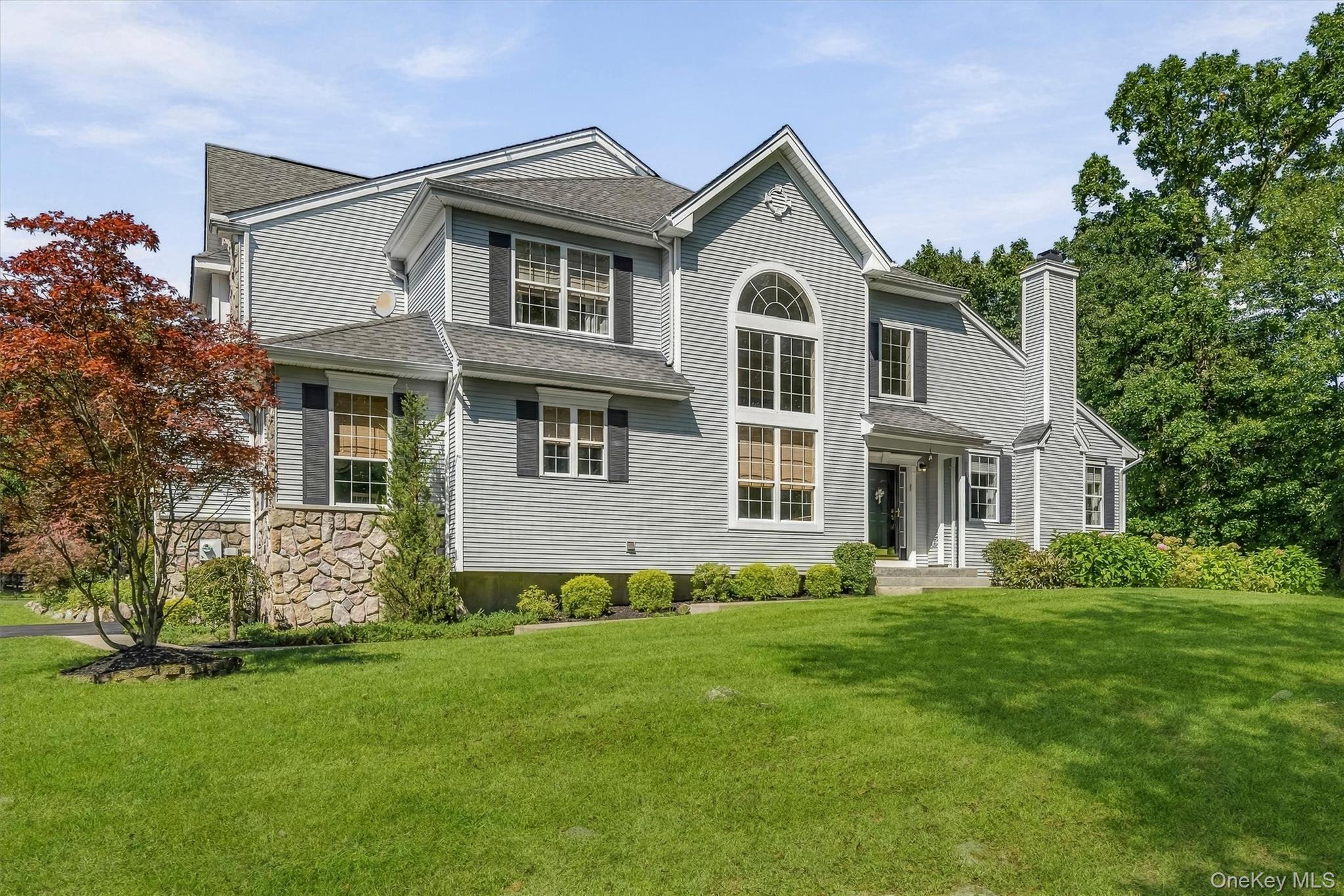 Gray two-story house with a stone foundation, arched window, and broad green lawn.