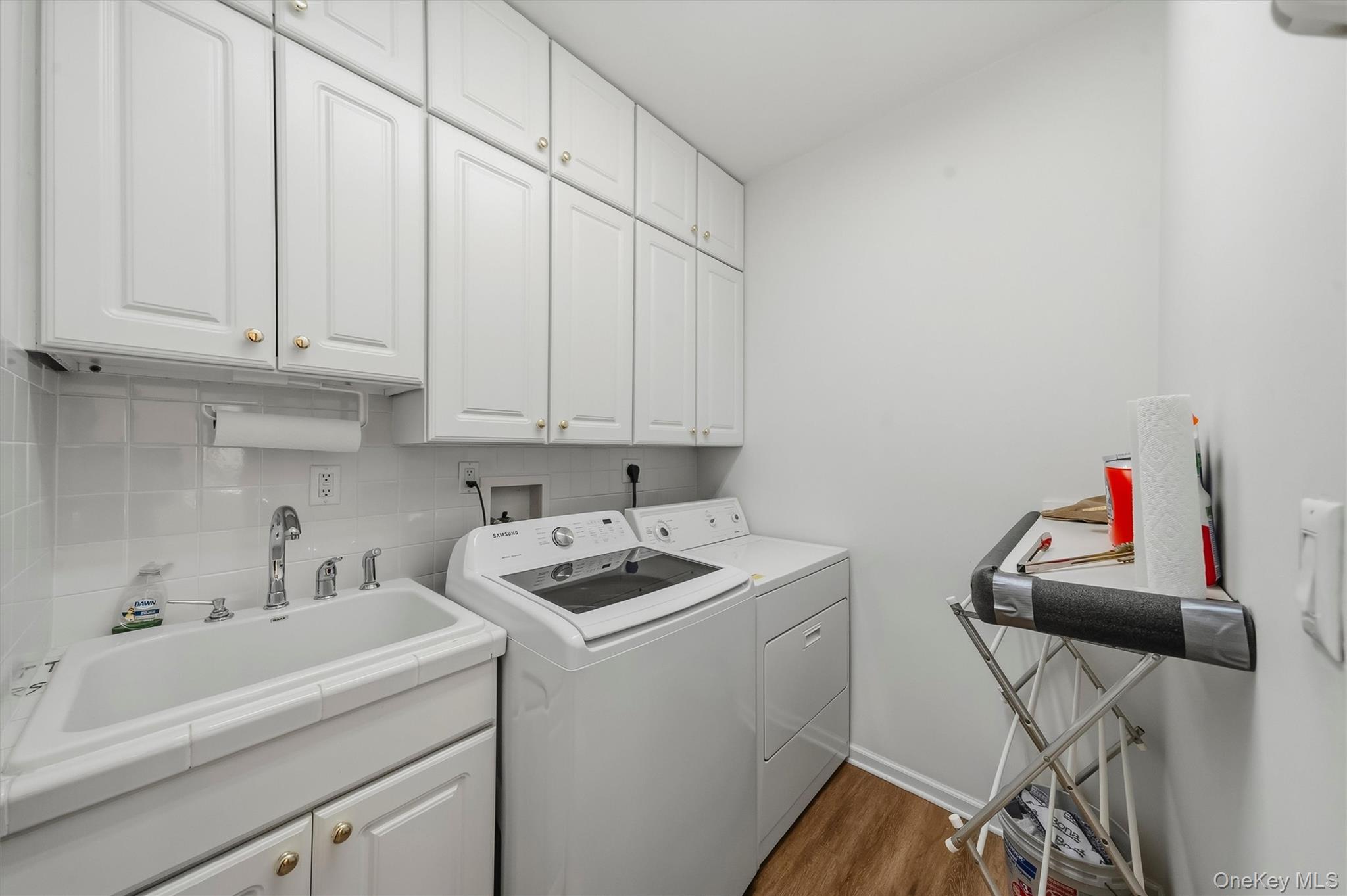 Laundry room with white cabinets, utility sink, washer, dryer, and ironing board.