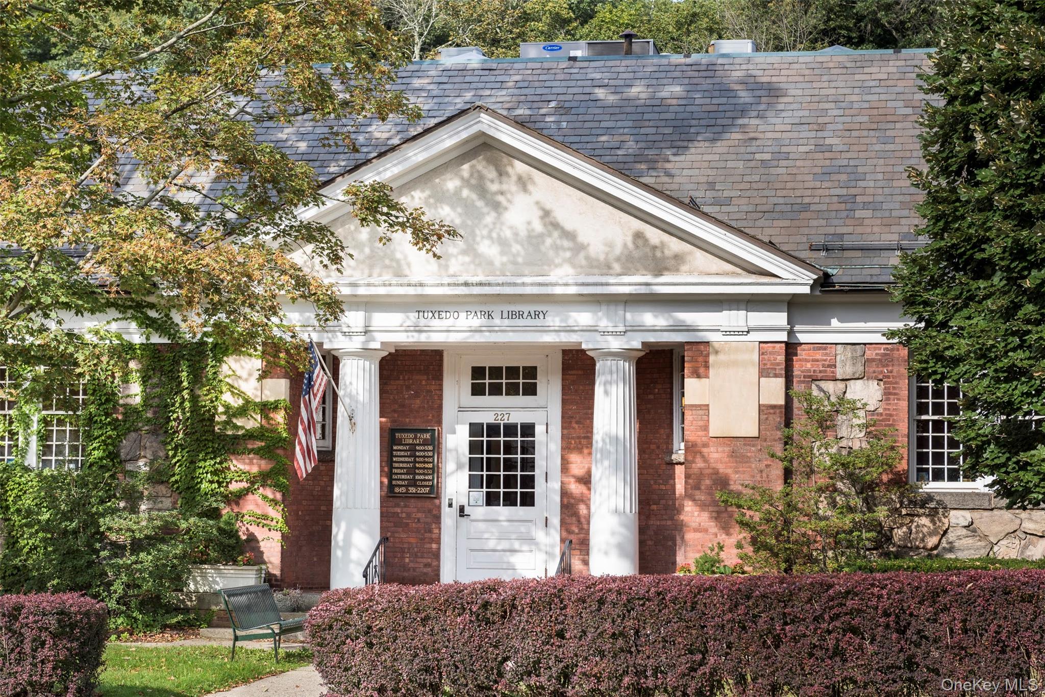 Tuxedo Park Library entrance with white columns, brick walls, and an American flag.