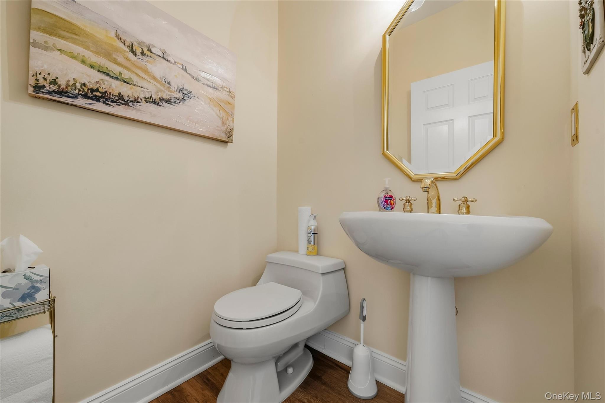 Bathroom with a white pedestal sink, gold fixtures, and a toilet beneath abstract wall art.