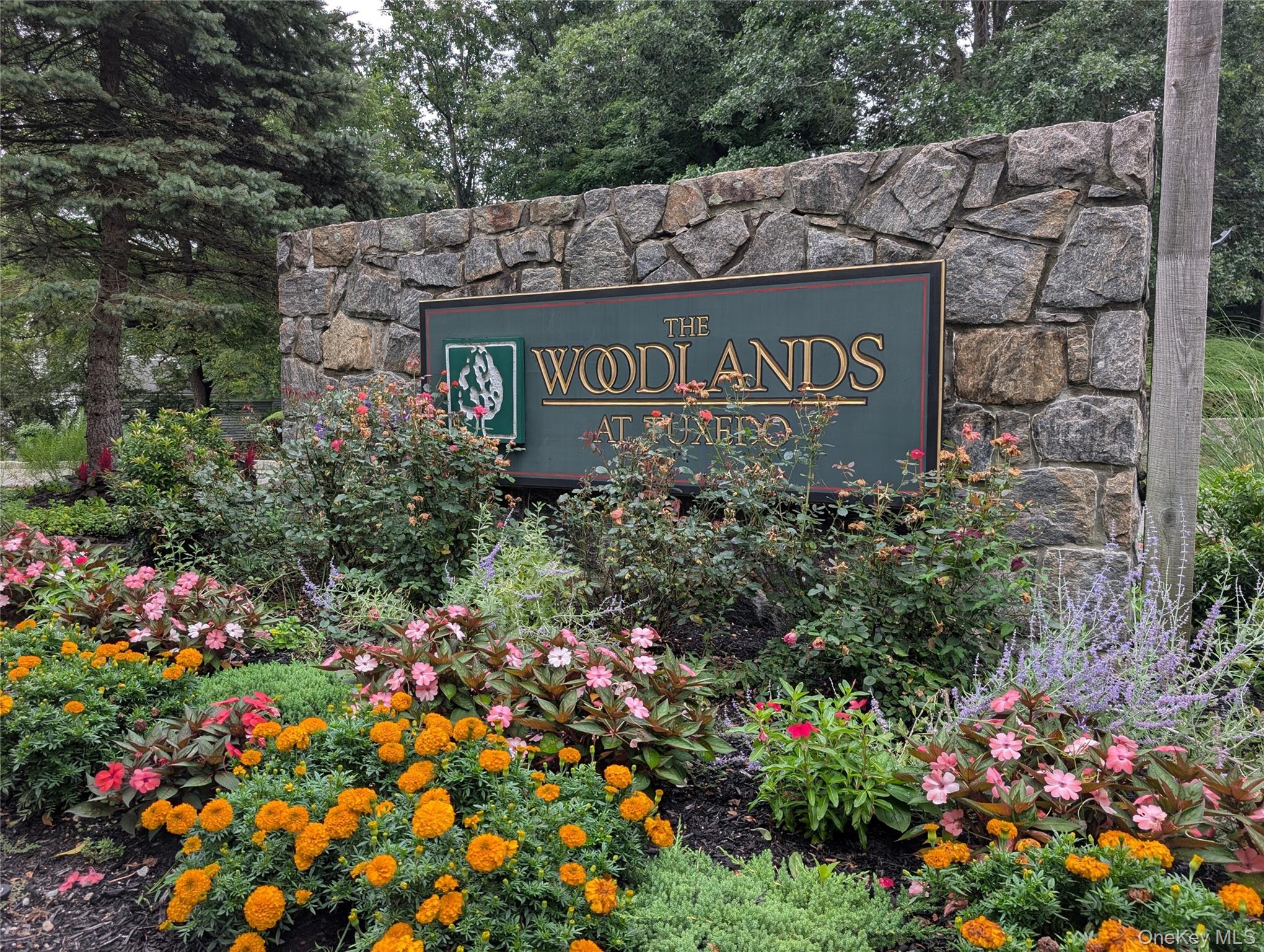 The Woodlands at Tuxedo entrance sign set in a stone wall among colorful flowers.