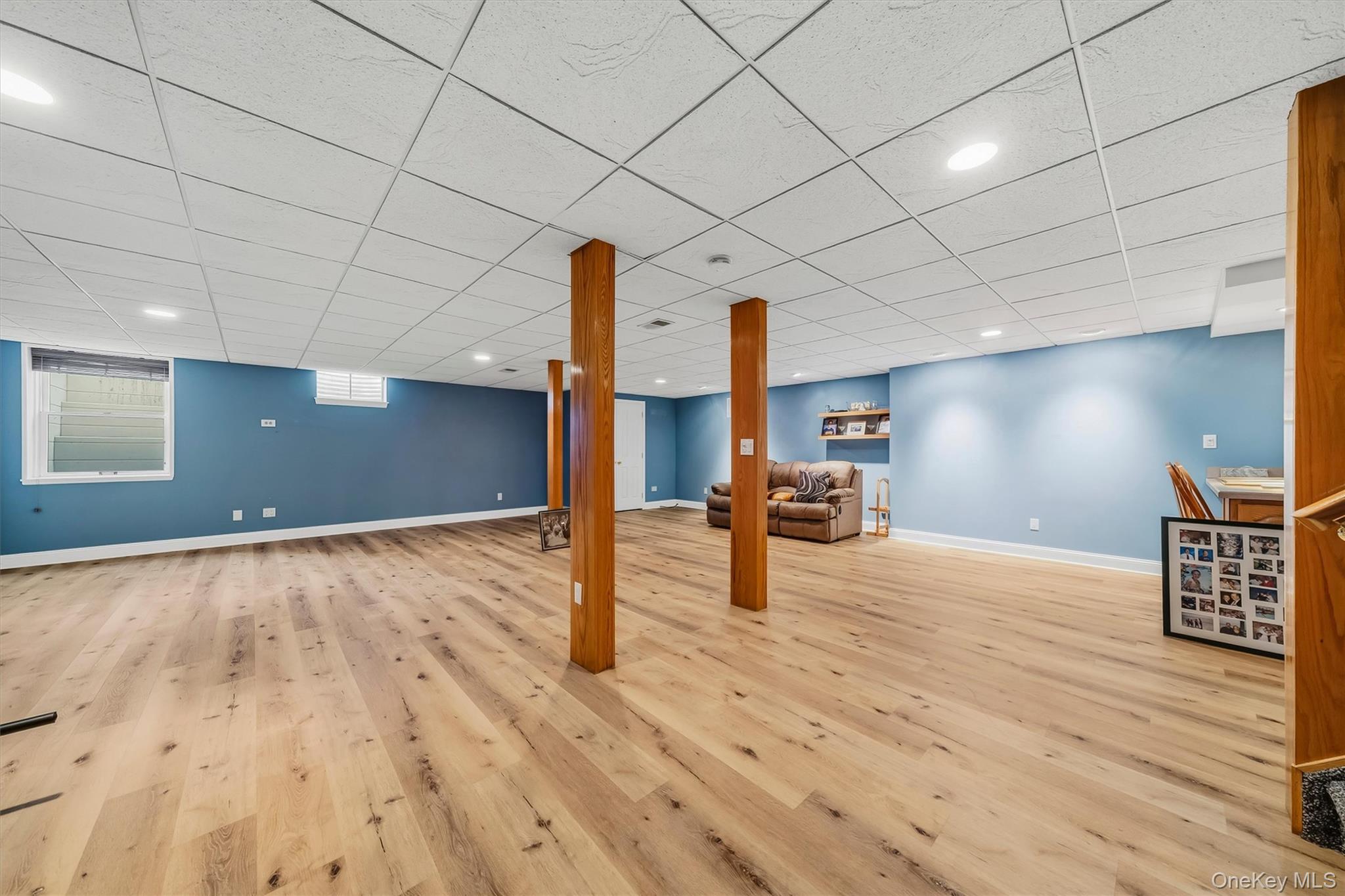 Finished basement family room with blue walls, light wood floors, and wooden support columns.