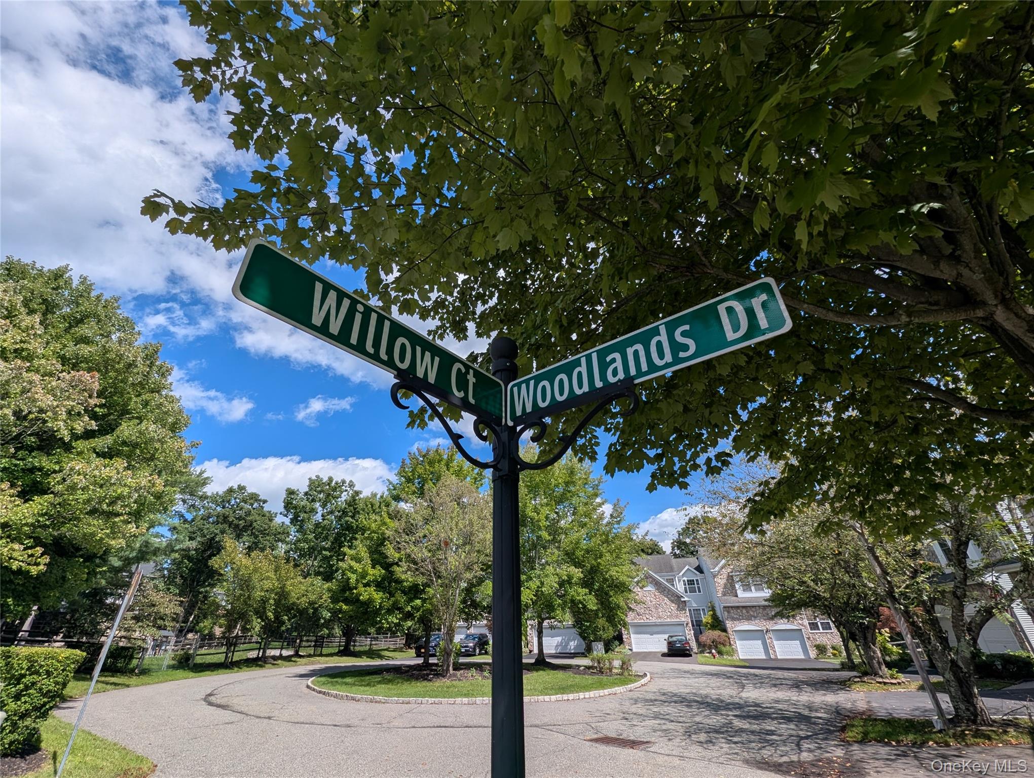 Residential intersection at Willow Ct and Woodlands Dr beneath leafy trees, with homes nearby.