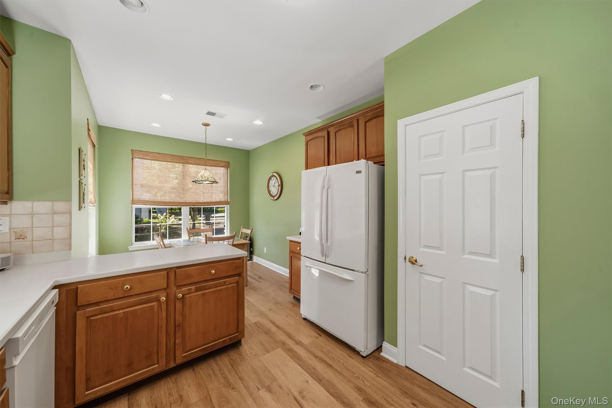 Kitchen with green walls, warm wood cabinetry, a white refrigerator, and a window-side dining area.