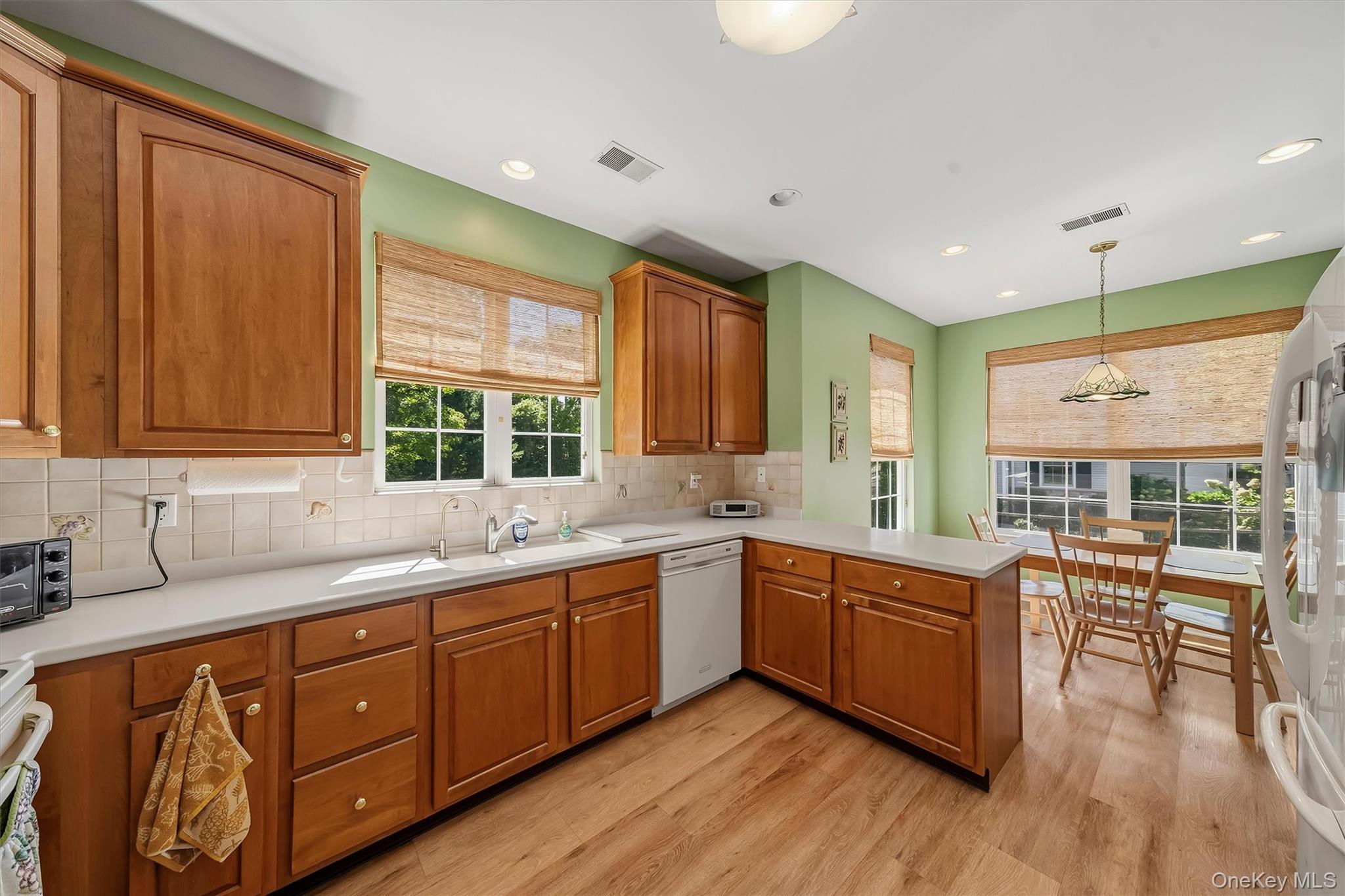 Kitchen with warm wood cabinets, white counters, green walls, and a window-side dining area.