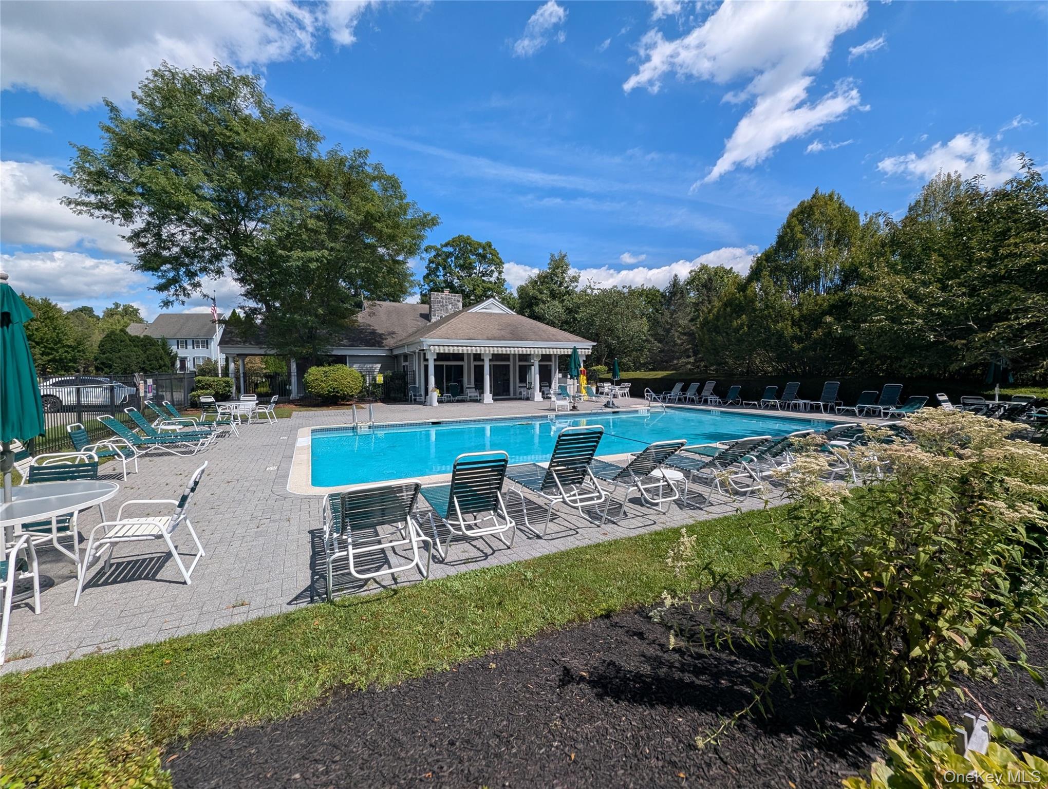 Community pool with a paved deck, rows of lounge chairs and a pavilion.