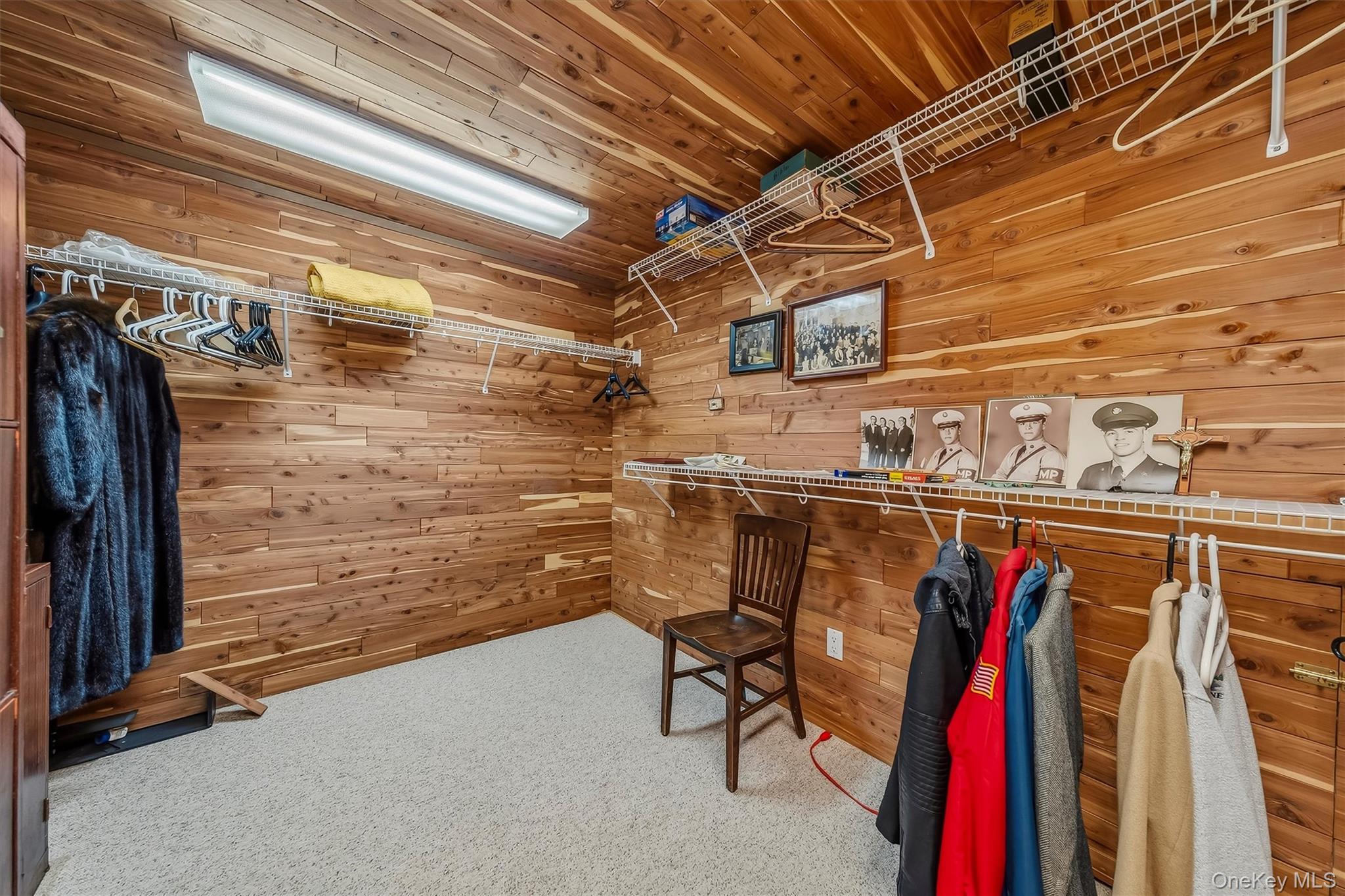 Wood-paneled walk-in closet with wire shelves, hanging clothes, and a wooden chair.