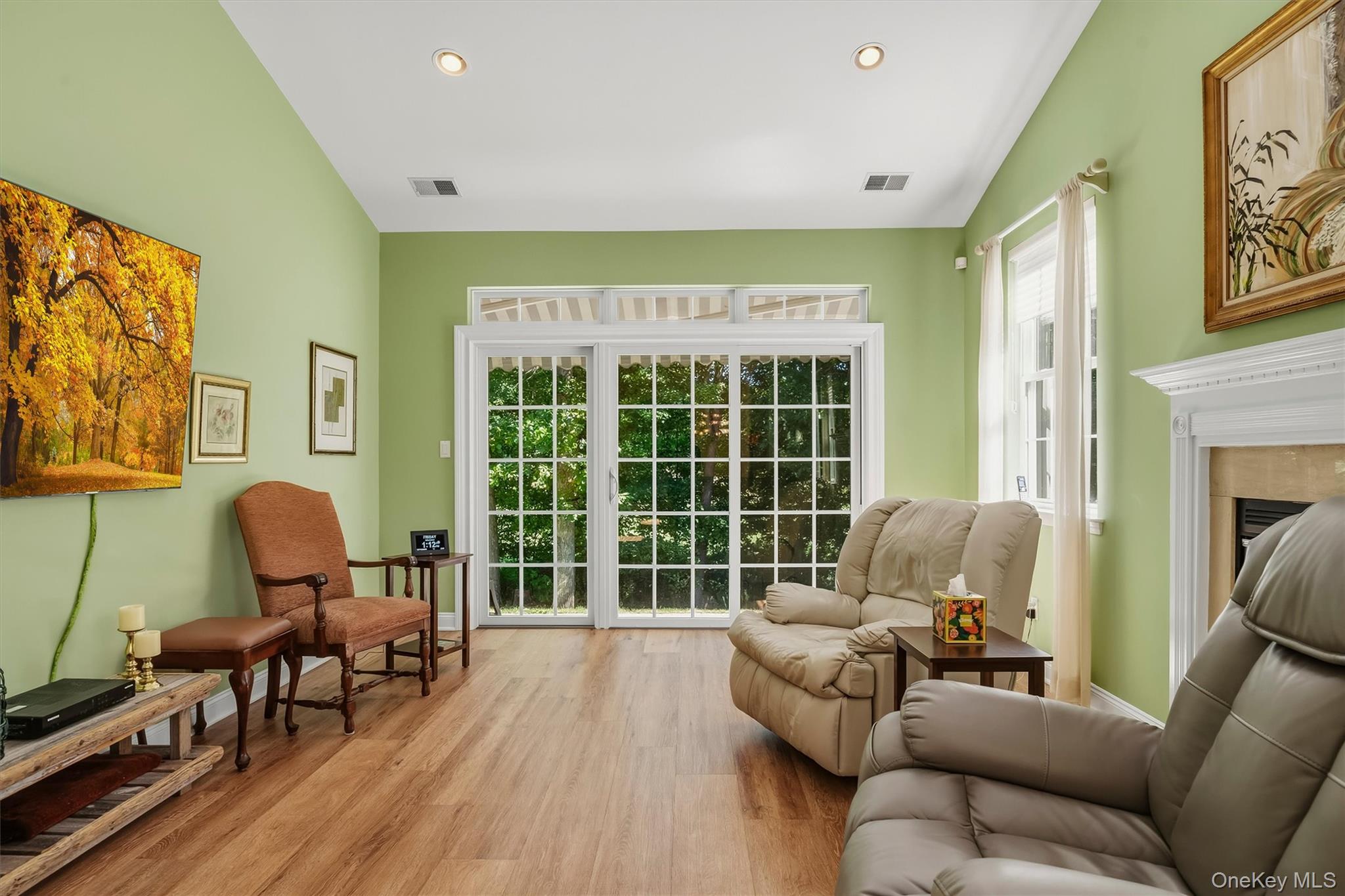Living room with green walls, beige recliners, wood floors, and large glass doors overlooking greenery.