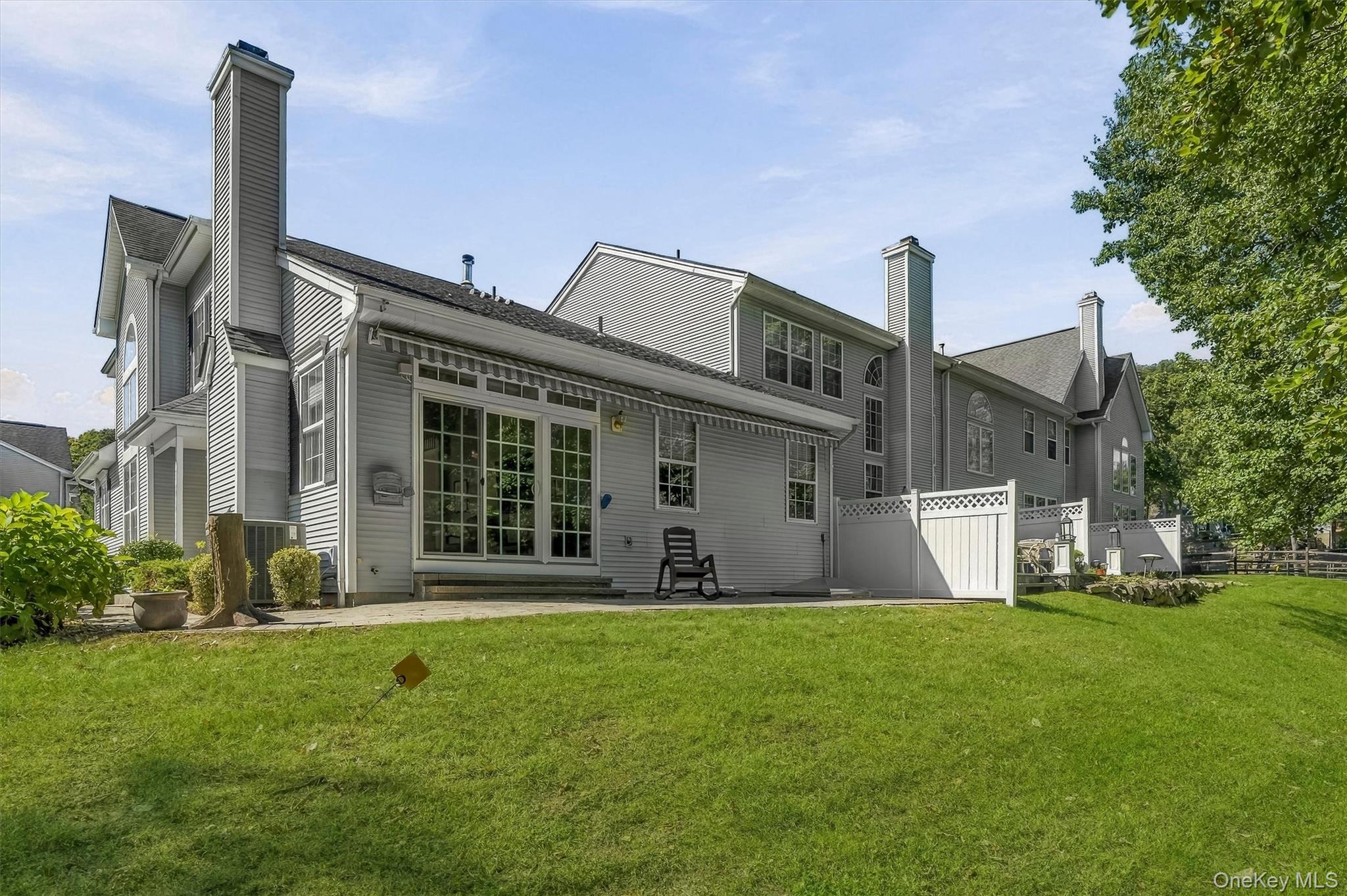 Rear exterior of a gray multi-story home with a fenced patio and broad green lawn.