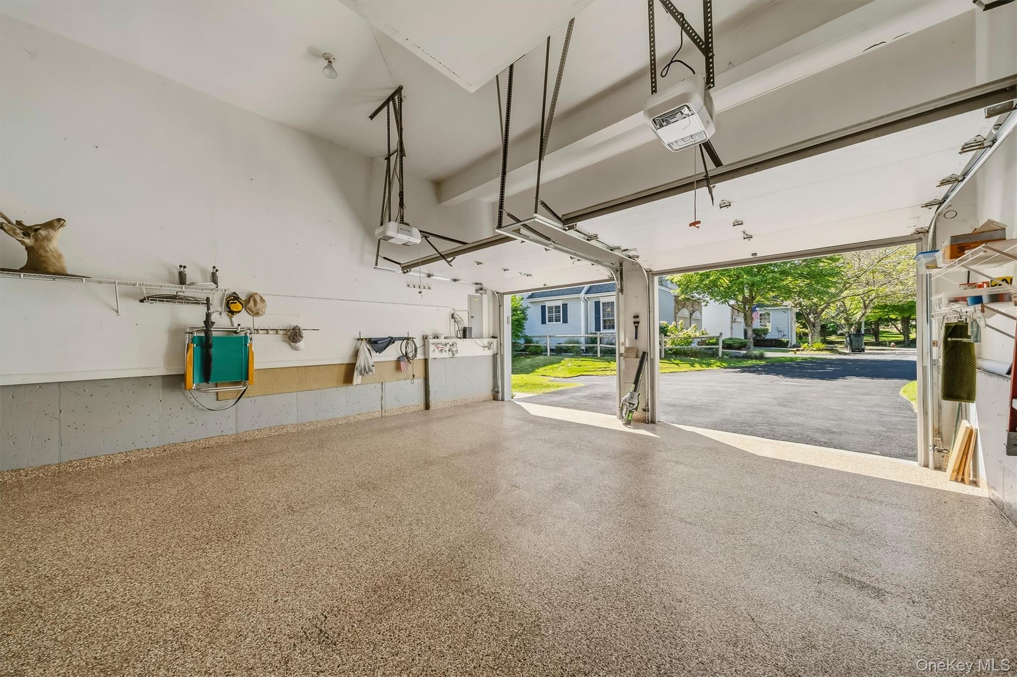 Garage with a speckled epoxy floor, wall storage, and open doors facing a sunny driveway.