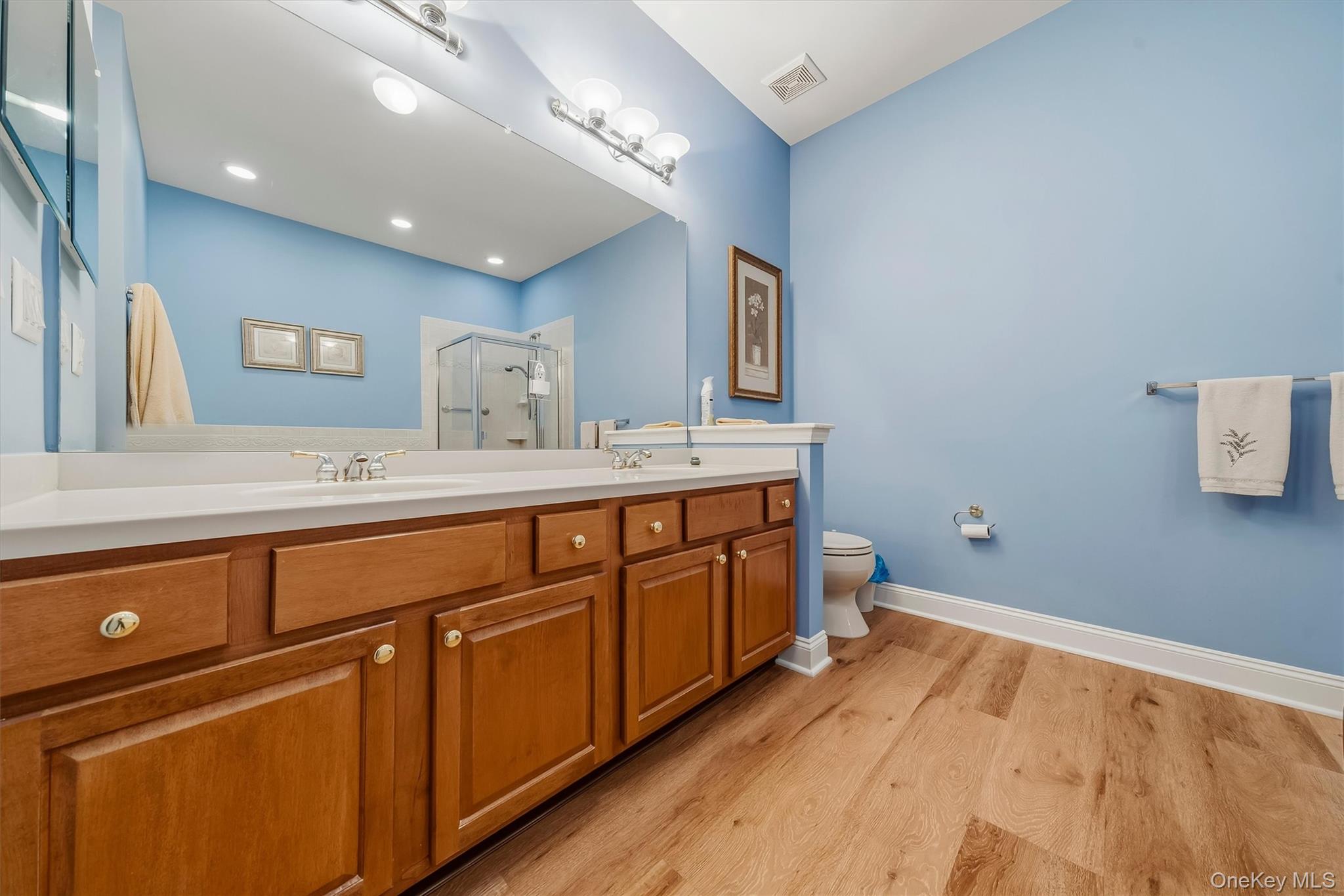 Bathroom with a long wood double vanity, blue walls, glass shower, and wood-look flooring.
