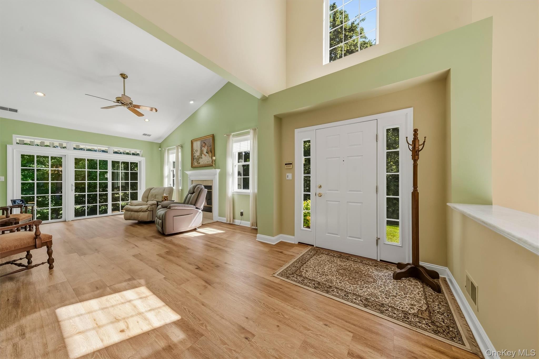 Furnished entry foyer with vaulted ceiling, hardwood floors, and large glass doors beside a sitting area.