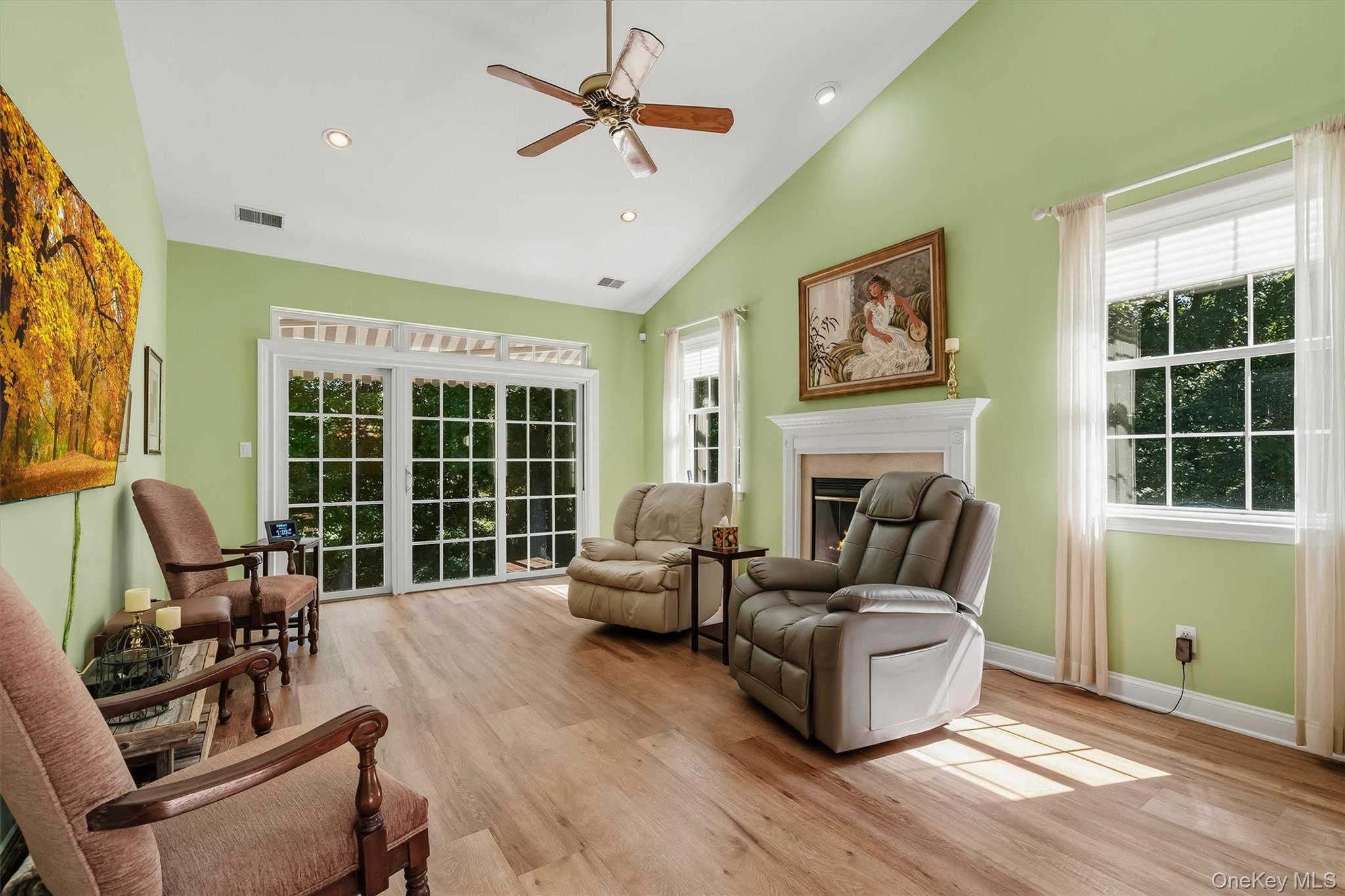 Living room with a white fireplace, reclining chairs, and large glass doors overlooking greenery.
