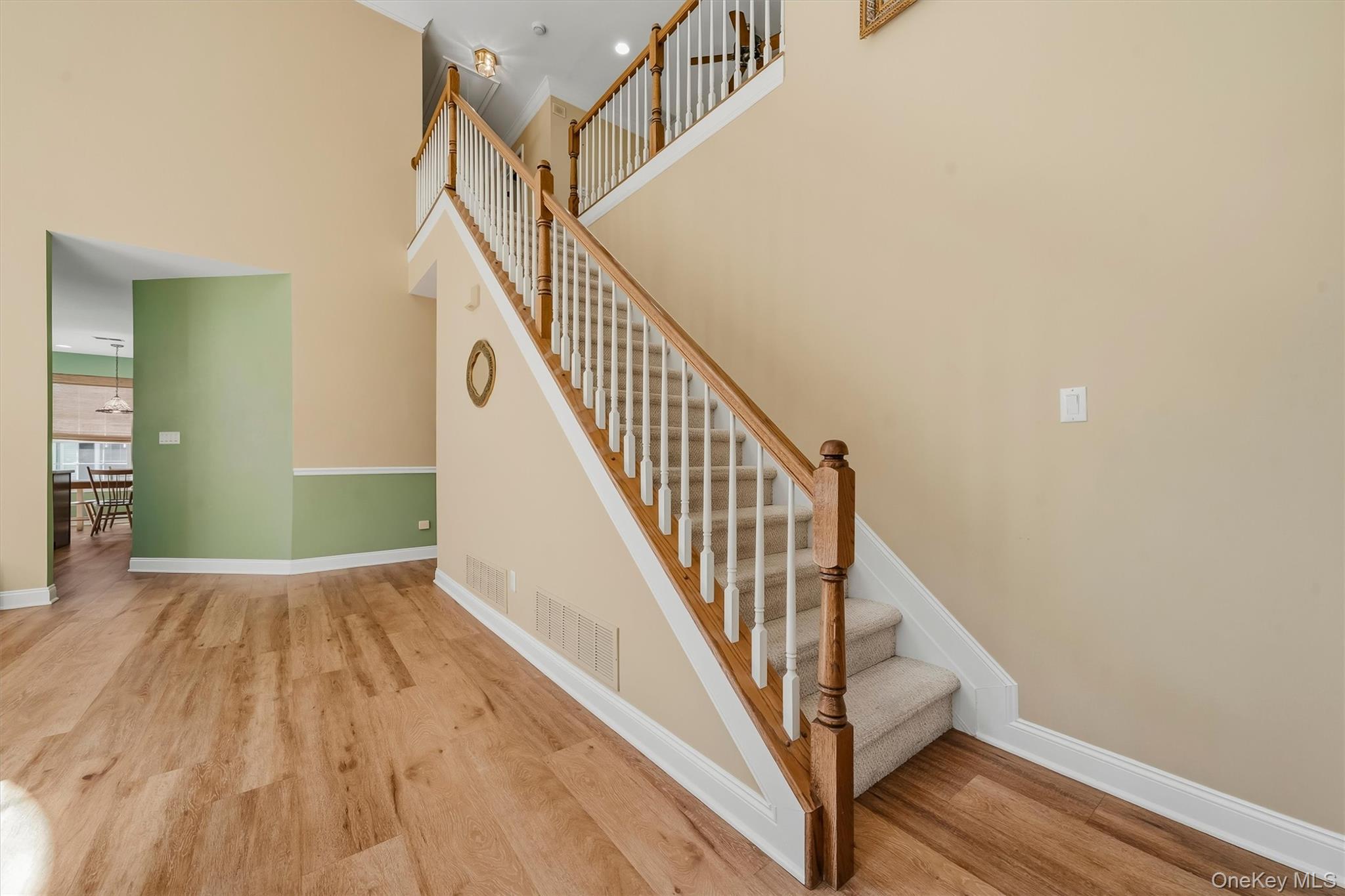 Foyer with a carpeted staircase, wood handrails, and wood-look flooring.