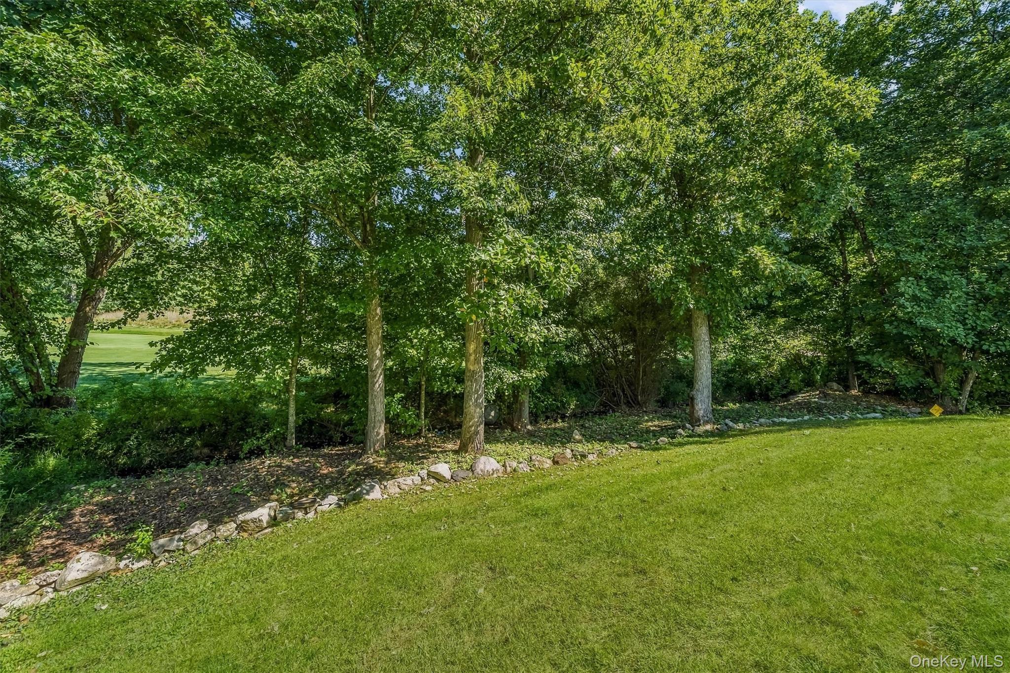 Green lawn bordered by mature trees and a low stone edging.