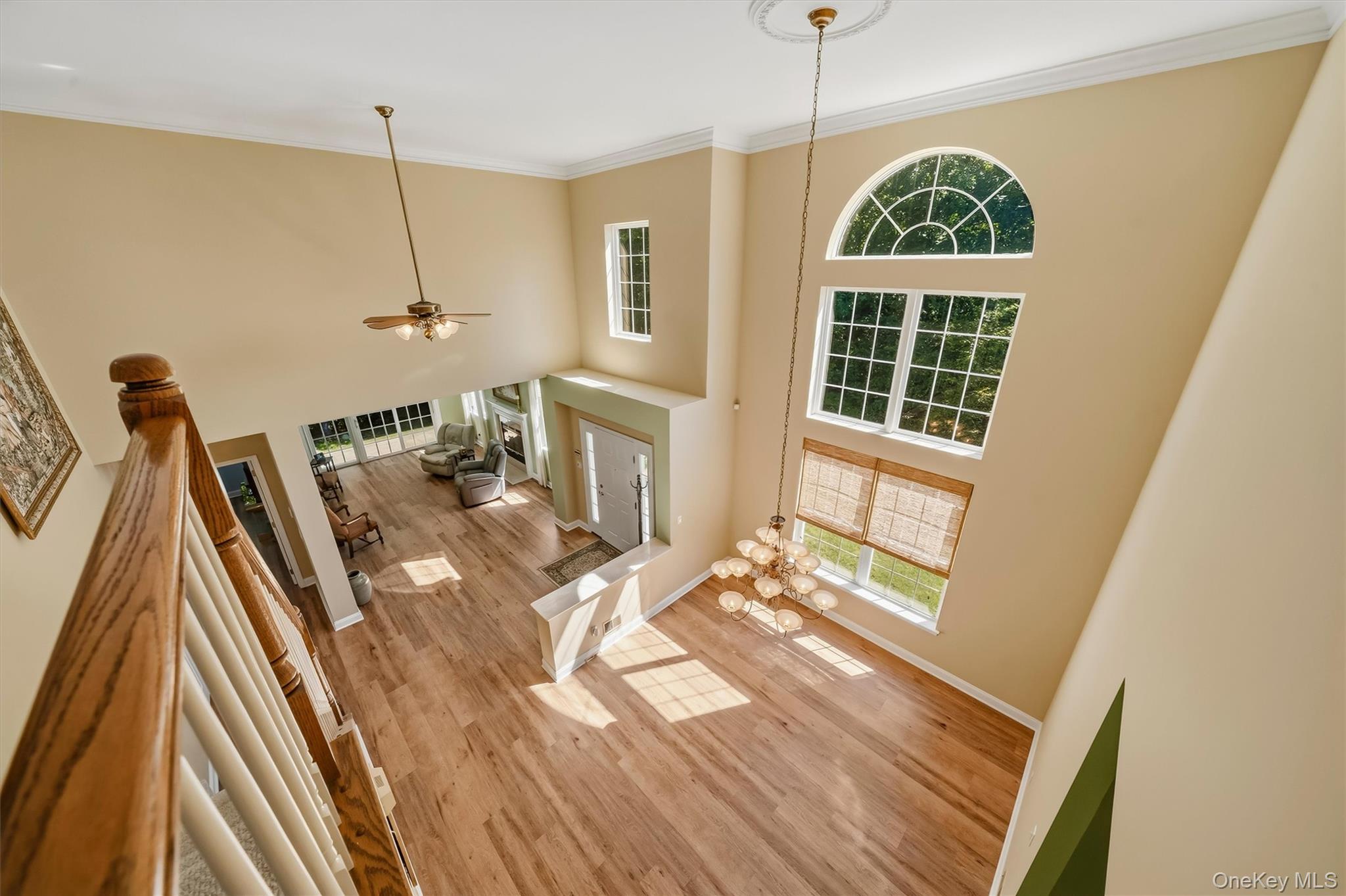 Two-story living room with tall arched windows, hardwood floors, chandelier, and a furnished sitting area.