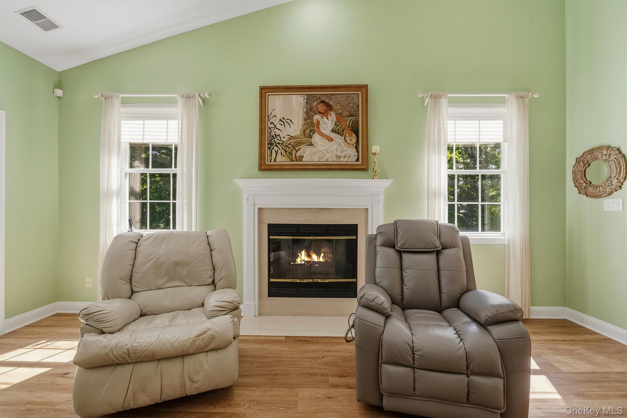 Living room with two leather recliners facing a lit fireplace between curtained windows.