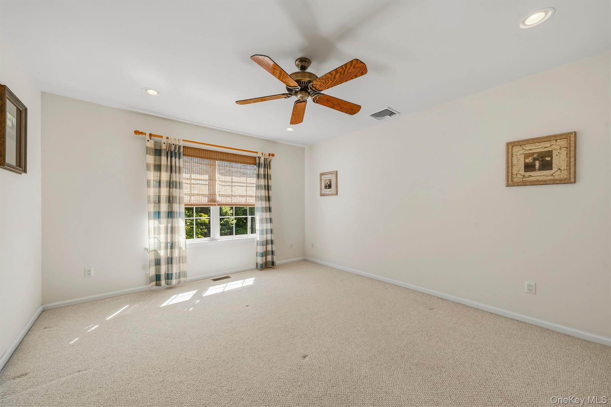 Vacant bedroom with beige carpeting, a wood-blade ceiling fan, and a curtained window.