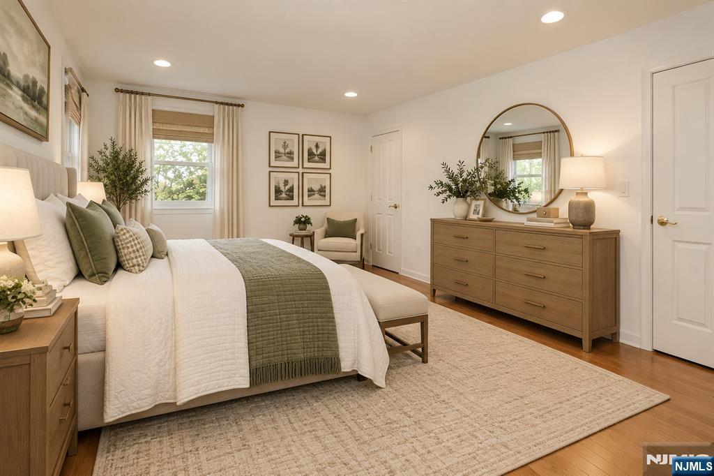 Staged bedroom with white bedding, an olive-green throw, and a wood dresser beneath a round mirror.