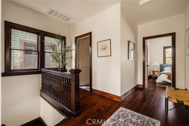 Interior landing with dark hardwood floors, ornate railing, tall windows, and a bedroom doorway.