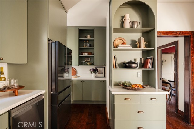 Kitchen with sage-green cabinetry, open display shelves, a stainless-steel refrigerator, and dark wood floors.