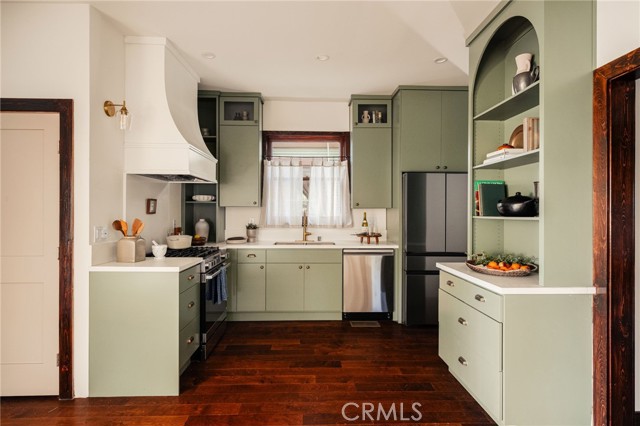 Kitchen with sage-green cabinets, dark hardwood floors, and a window above the sink.