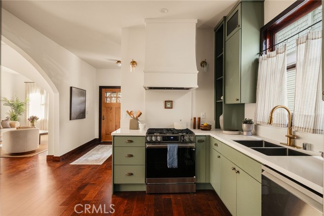 Kitchen with sage-green cabinets, a farmhouse sink, brass faucet, and dark hardwood floors.