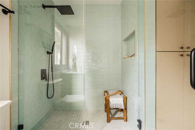 Walk-in shower with pale green tile, glass panels, and a wooden stool with towels.