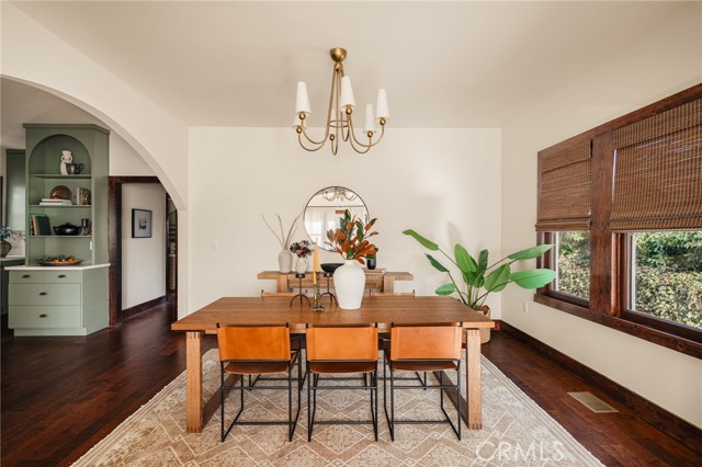 Dining room with a long wooden table, patterned rug, built-in green cabinet, and large windows with wooden blinds.
