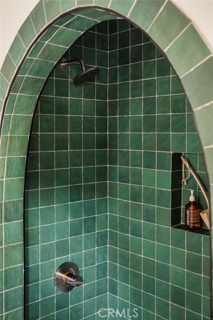 Arched shower with deep green tile, a rainfall showerhead, and a built-in toiletries niche.
