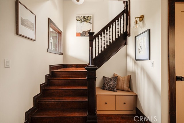 Dark wood staircase with turned balusters beside a built-in bench with cushions.