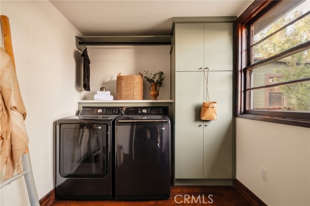 Laundry room with black washer and dryer, pale green cabinets, and a large window.